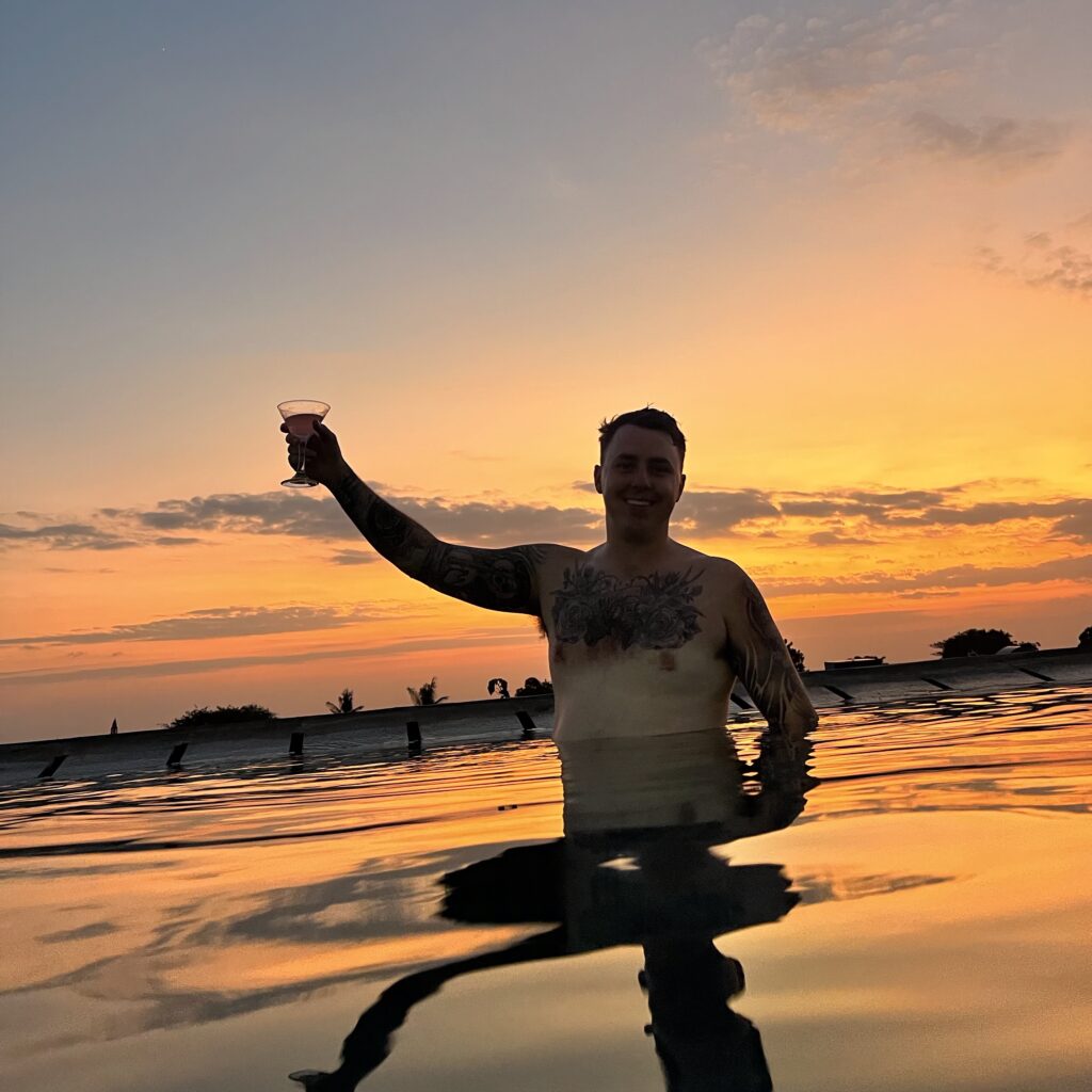 Jayden enjoying a rooftop pool in Bali at sunset, holding a cocktail with essential Bali travel tips for a perfect getaway.