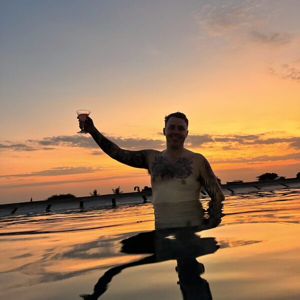 Jayden enjoying a rooftop pool in Bali at sunset, holding a cocktail with essential Bali travel tips for a perfect getaway.